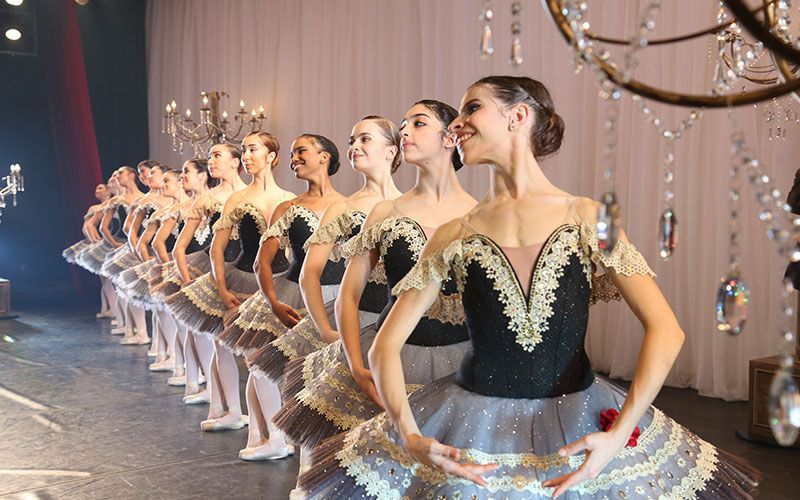 Um grupo de bailarinas estão em fila no palco.