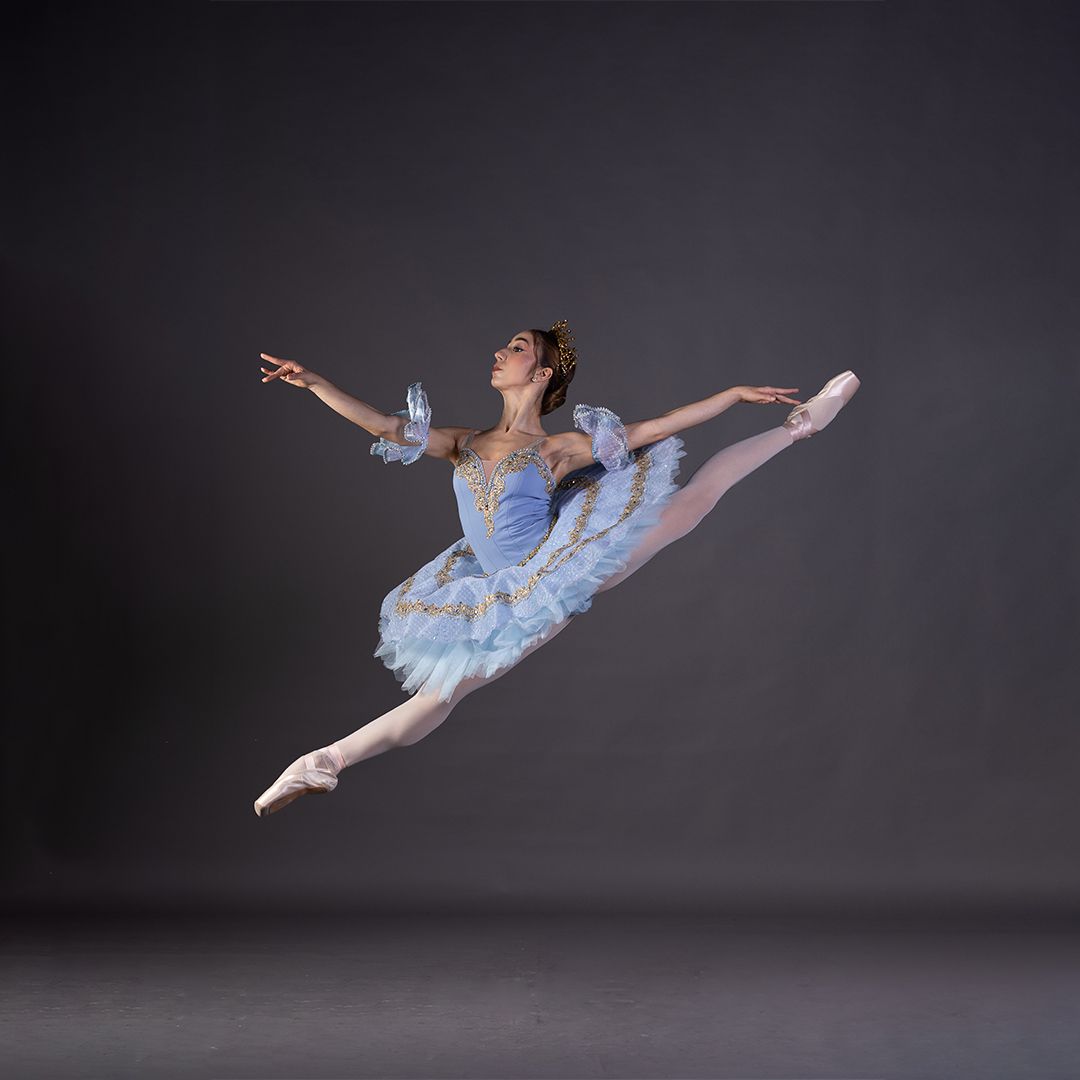 Uma bailarina com um tutu azul está pulando no ar.
