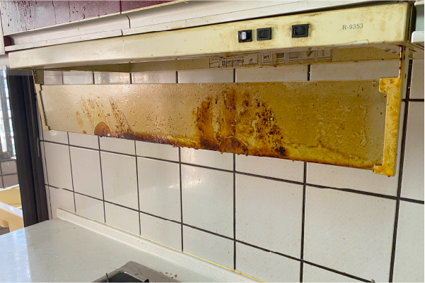 油煙機上積滿了厚厚的油污，擋水板上是白色的磁磚。