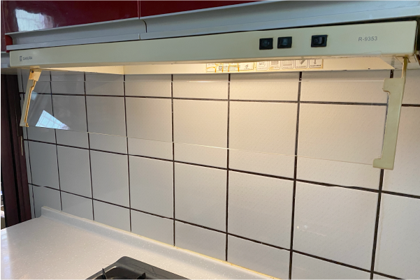 抽油煙機位於白色磁磚防濺板和檯面上方。抽油煙機上安裝了兩個透明塑膠防護罩。