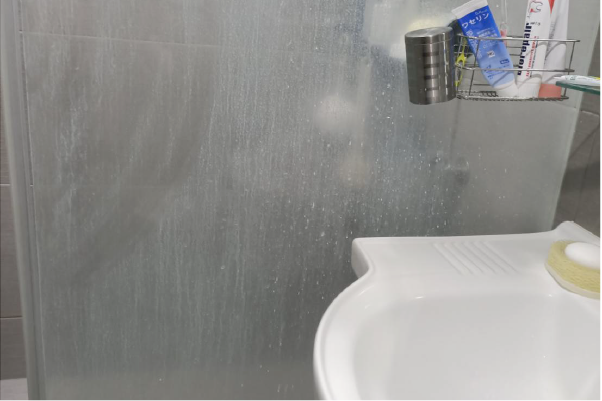 淋浴房門上蒙著霧氣，角落白色水槽旁放著牙膏和肥皂。