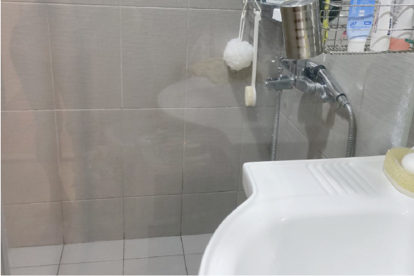 浴室內部：白色水槽、淋浴裝置、灰色瓷磚牆、架上的盥洗用品。