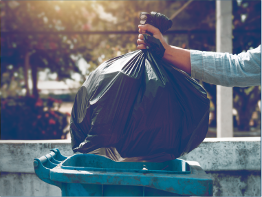 有人將黑色垃圾袋放入藍色戶外垃圾桶。