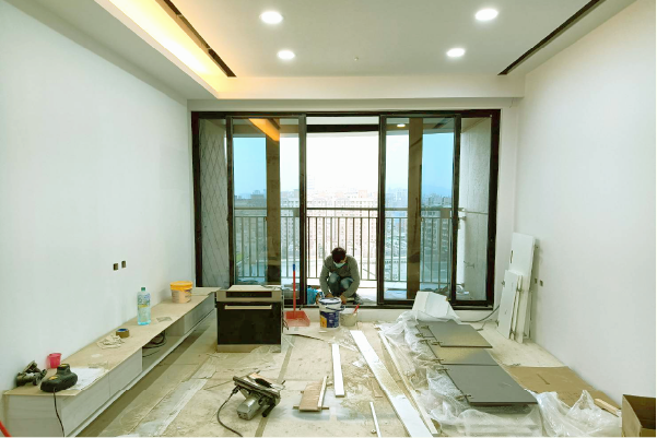 一名工人在明亮現代的客廳鋪設地板，客廳有大型滑動玻璃門和白色牆壁。