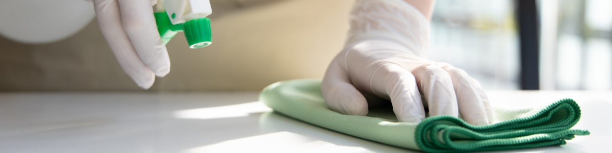 一隻戴著手套的手拿著噴霧瓶，用綠布擦拭表面。