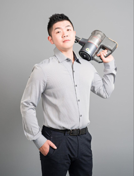 一名身穿襯衫的男子肩扛無線吸塵器，背景為灰色。