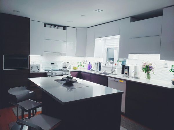 A modern kitchen featuring white cabinets, dark base units, a large island with bar stools, and under-cabinet lighting.