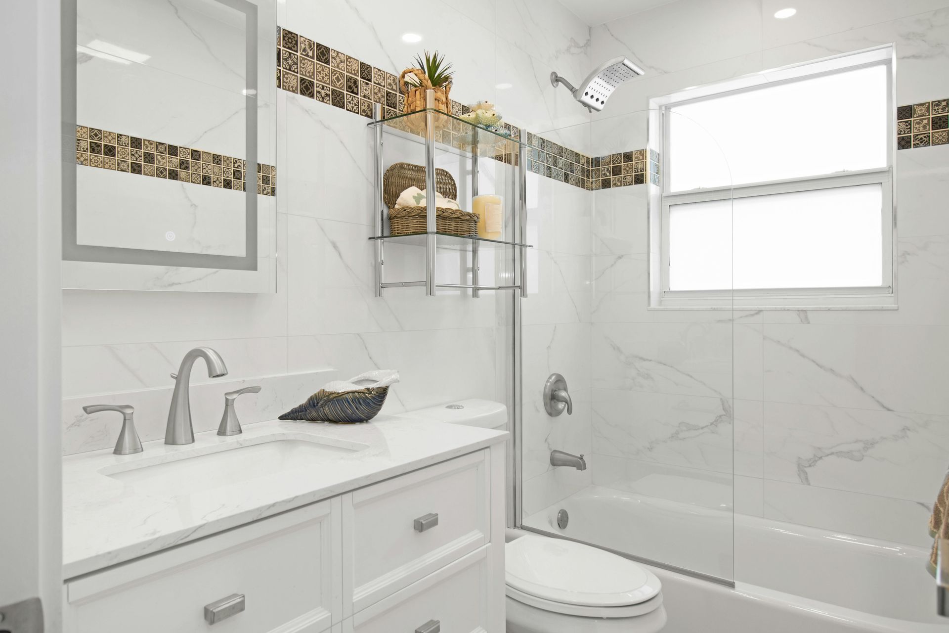 A modern bathroom with white marble-style wall tiles, a white vanity, a glass-enclosed shower, and decorative border tiles.