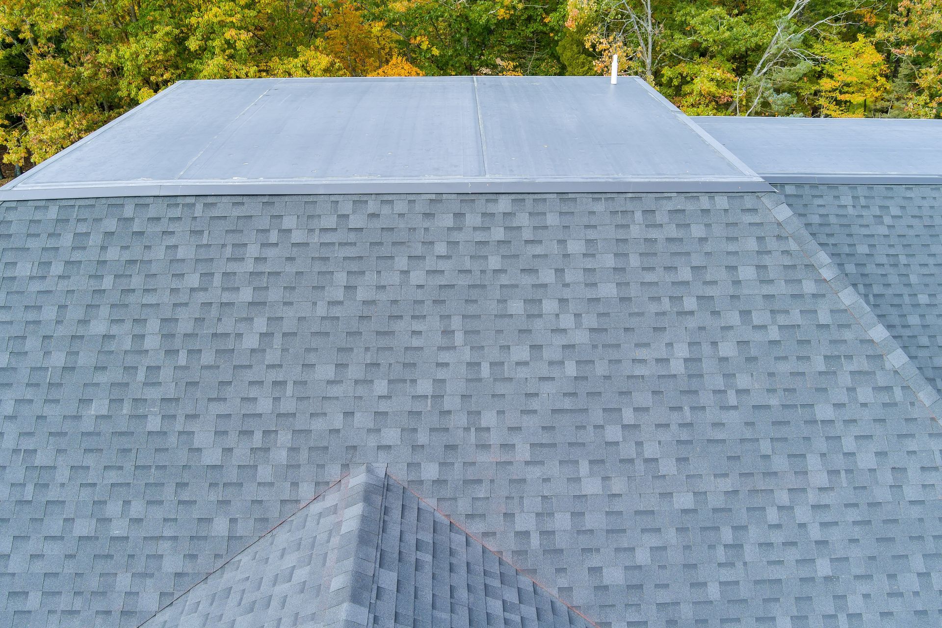 An aerial view of a dark shingled residential roof with a large, flat, light-gray panel section near the top.