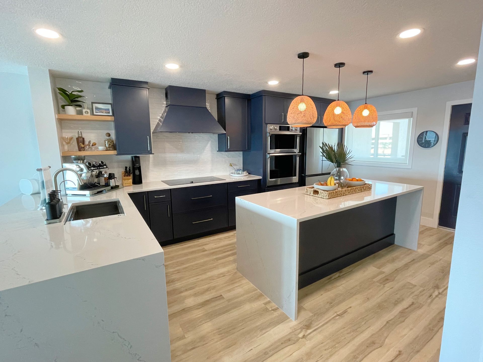 A modern kitchen with navy blue cabinetry, white quartz countertops, a large island, and three pendant lights.