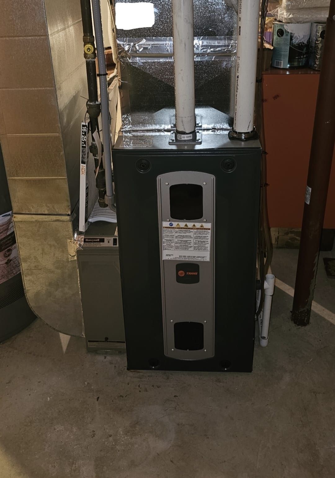 Dark green furnace in a basement. White pipes attached, concrete floor.