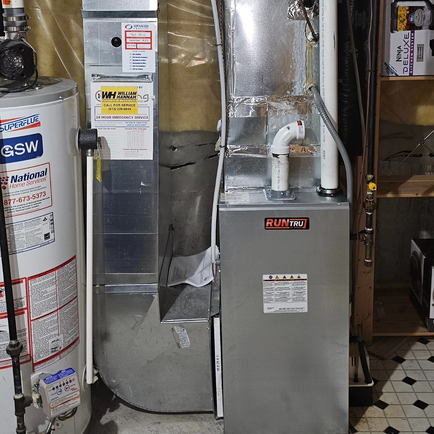 Water heater and furnace in a basement, metal and white fixtures, grey concrete wall.