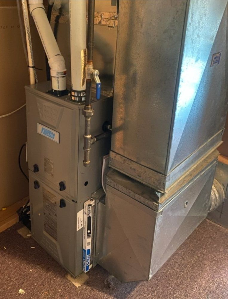 A furnace in a basement with silver metal casing, ducts, and white PVC pipes.