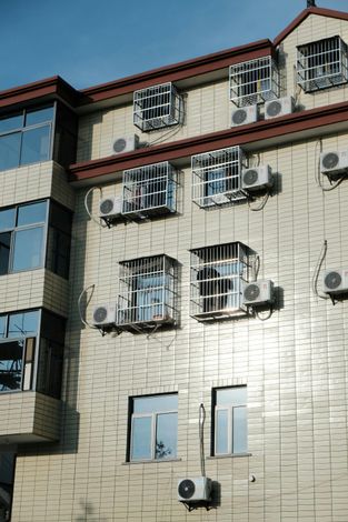 Building exterior with windows, security bars, air conditioners. Light-colored brick with a red roof.