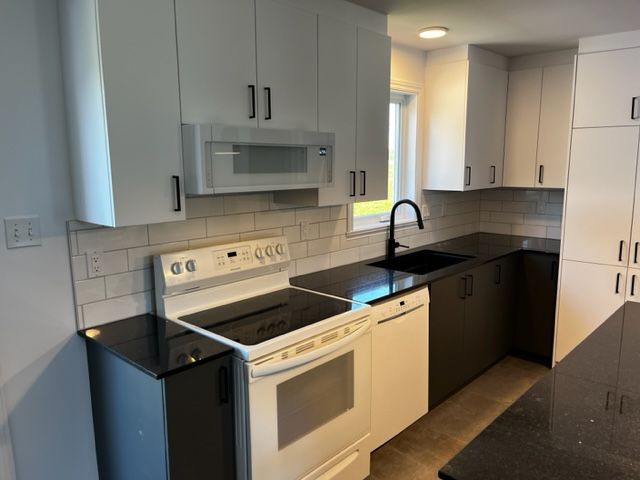 Une cuisine avec des armoires blanches et des comptoirs noirs