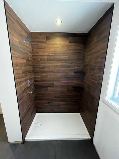Une cabine de douche avec un mur en bois et un receveur de douche blanc.