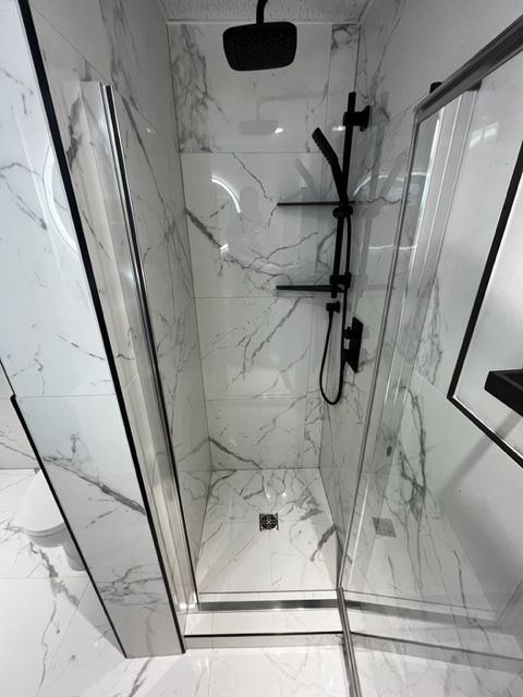 Une salle de bain avec carrelage en marbre et une douche à l'italienne avec pommeau de douche noir.