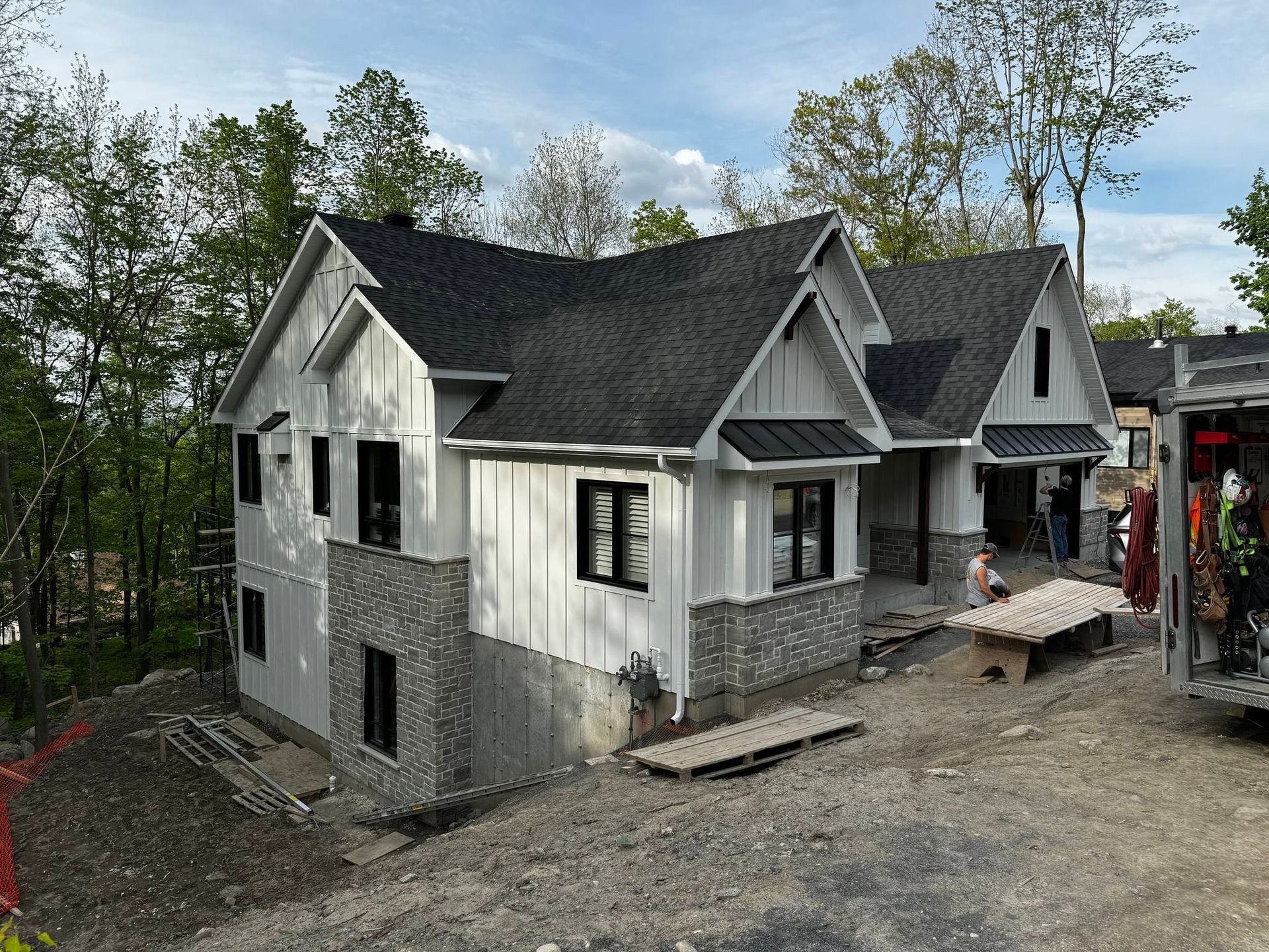 Nouvelle maison en construction avec revêtement blanc, toit noir et accents de brique.