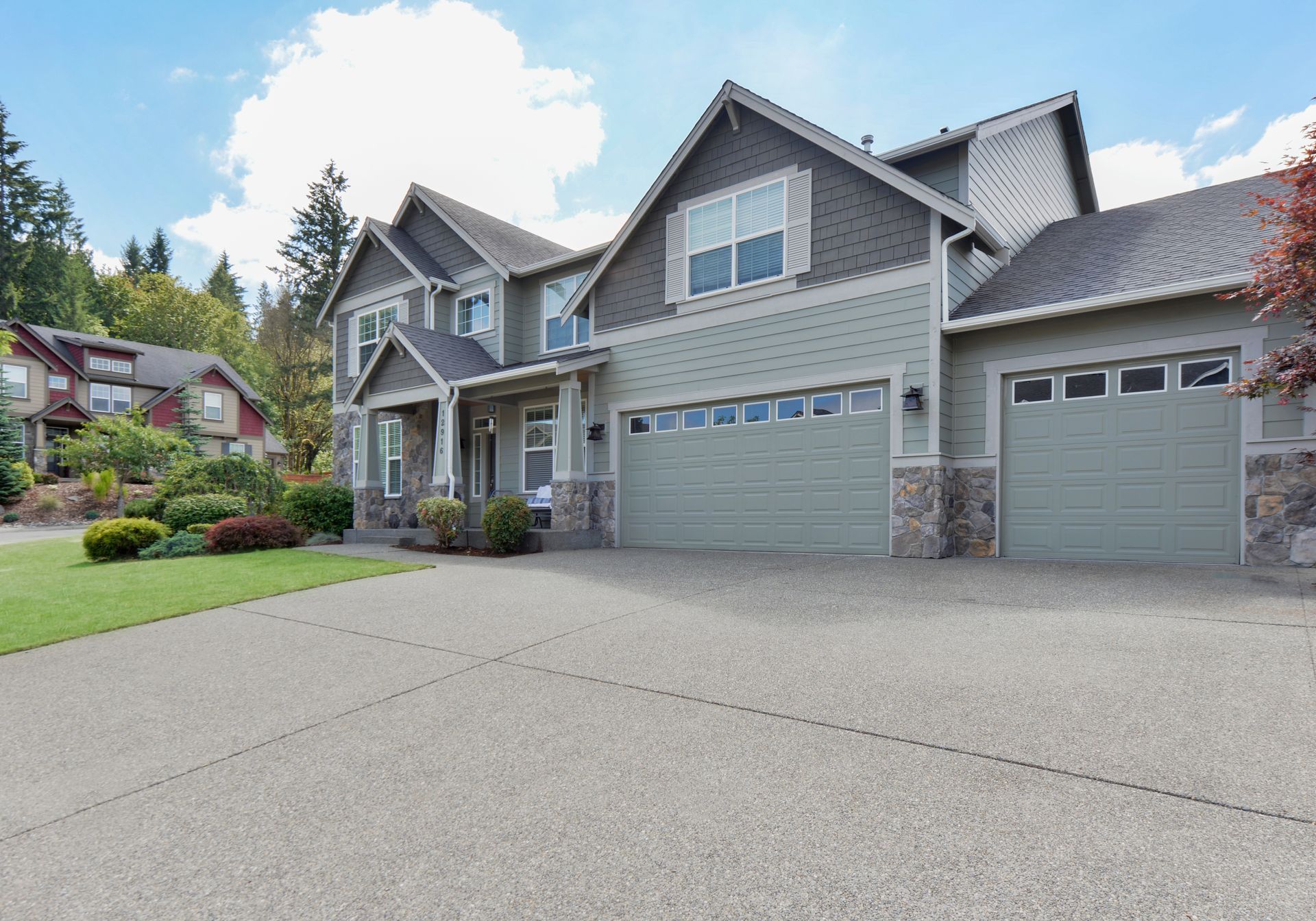 Maison à deux étages avec une grande allée et un revêtement vert sous un ciel bleu.