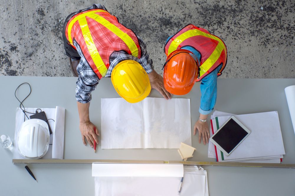 Deux ouvriers du bâtiment regardent un plan sur une table.