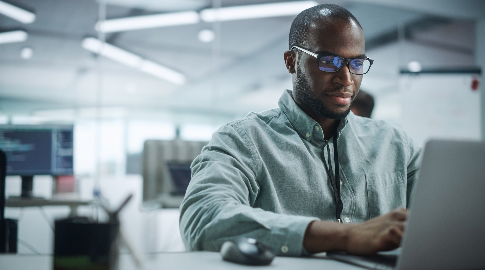 A man wearing glasses is sitting at a desk using a laptop computer.