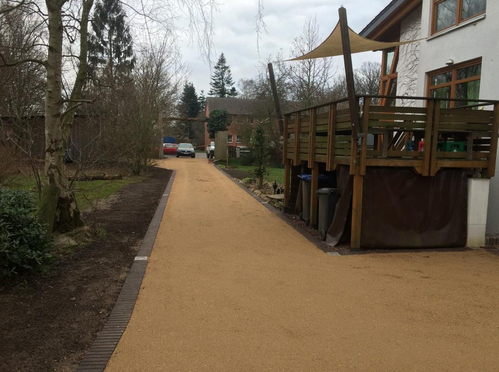 Camino de grava que conduce a un edificio con terraza de madera y un coche aparcado en la distancia.