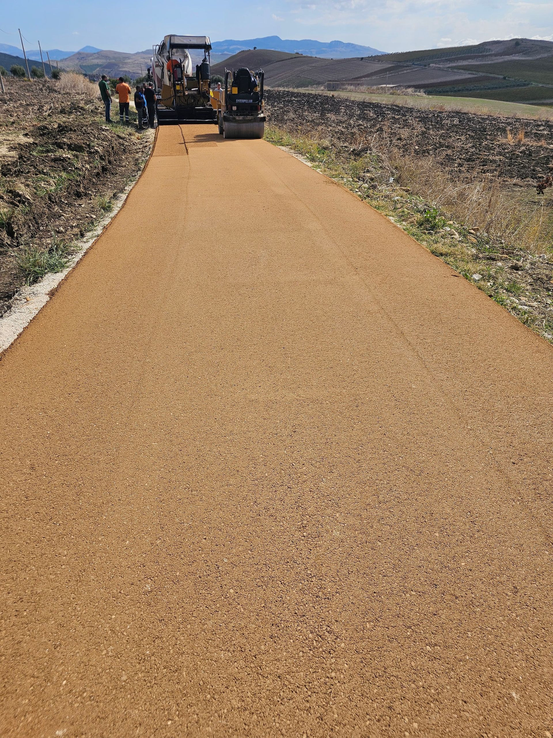 Construcción de un camino de ripio con maquinaria y trabajadores en una ladera.
