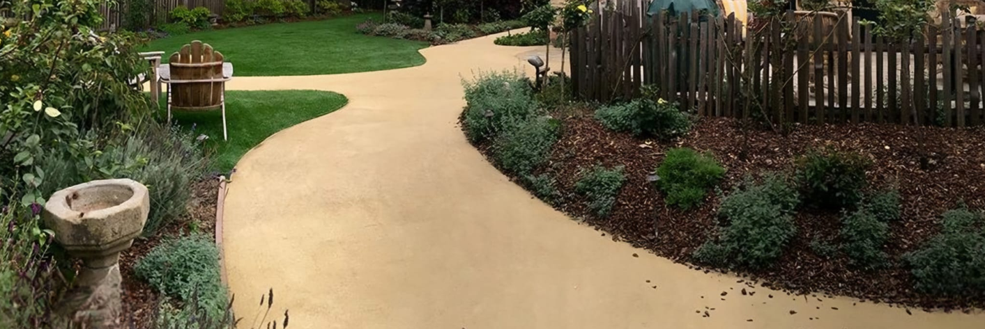 Un sendero sinuoso que atraviesa un jardín con una valla de madera y diversas plantas.