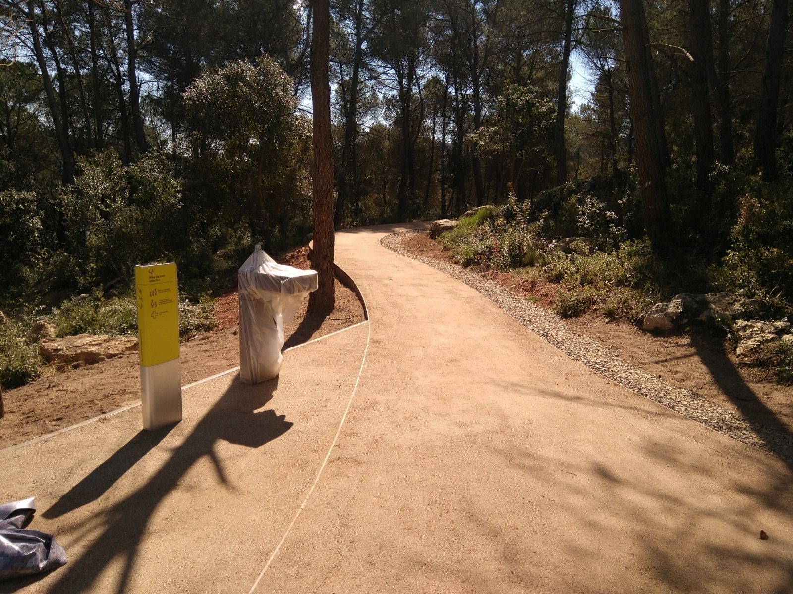 Persona lavando una superficie amarilla con una manguera al aire libre, con un automóvil y un paisaje de fondo.
