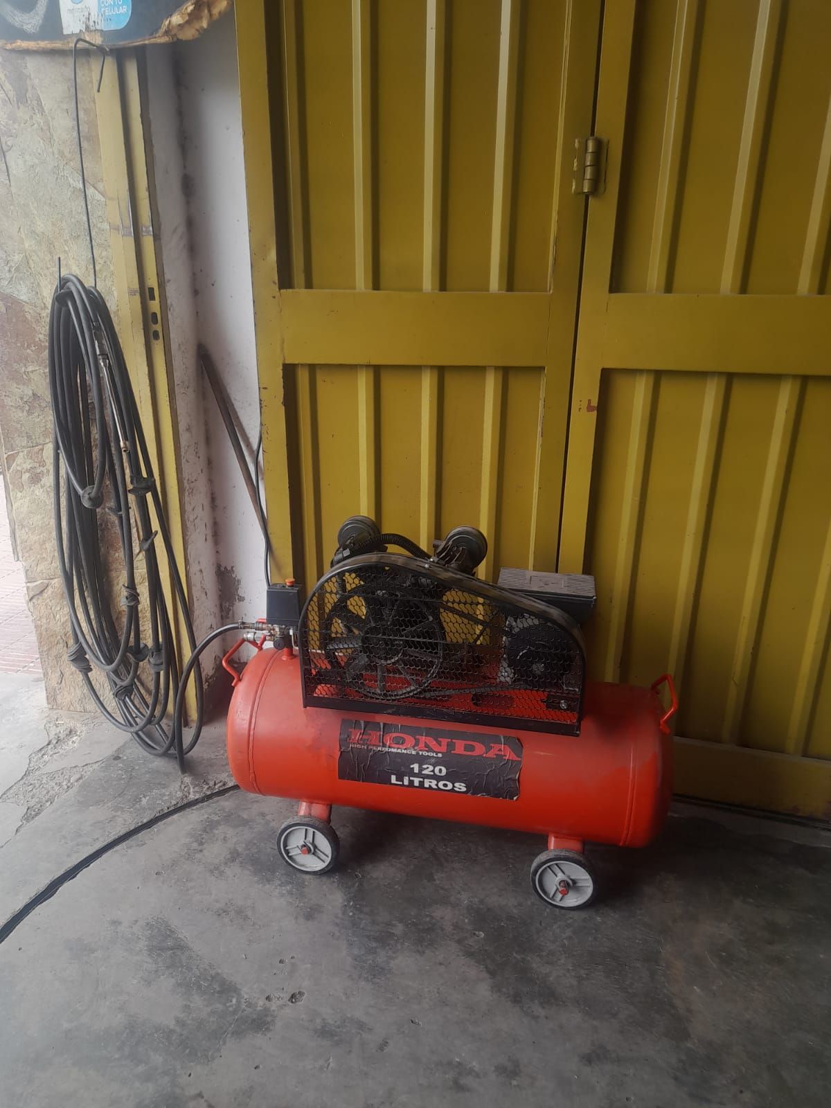 Compresor de aire Honda rojo sobre ruedas, al lado de una puerta amarilla.