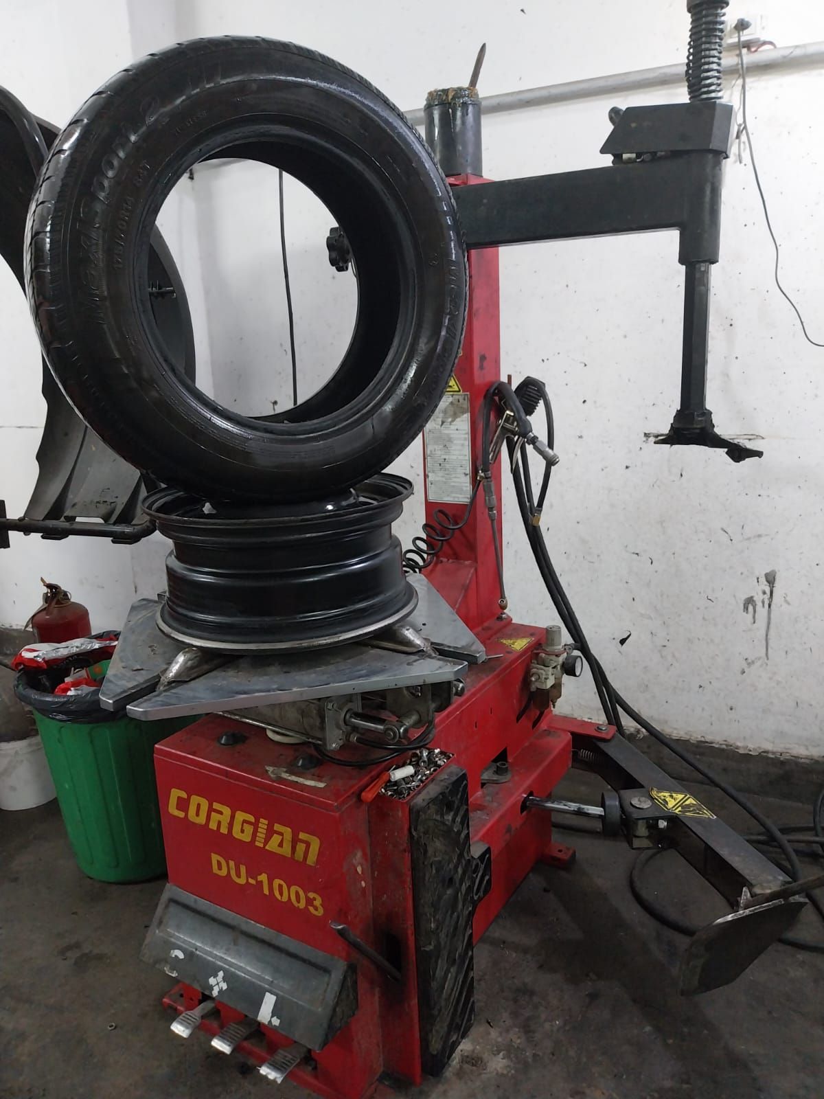 Un neumático que se monta en una llanta utilizando una máquina de cambio de neumáticos roja y negra en un garaje.