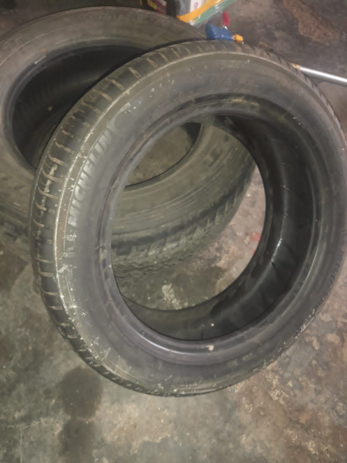 Dos neumáticos de coche desgastados, de goma negra, sobre un suelo oscuro.