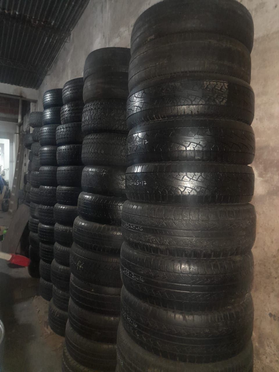 Pilas de neumáticos negros usados dentro de un área de almacenamiento poco iluminada.