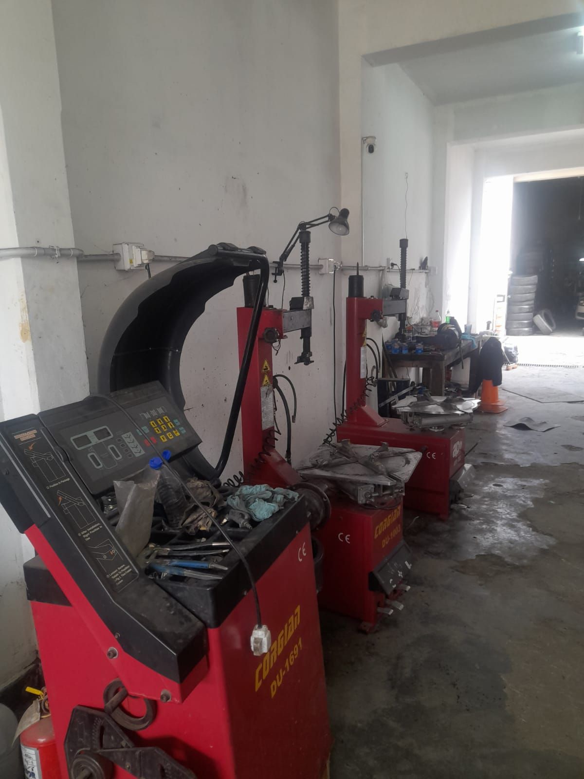 Interior de un taller de neumáticos con maquinaria roja. Una balanceadora de neumáticos en primer plano y dos desmontadoras.