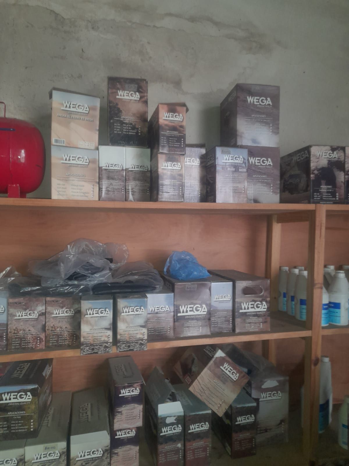 Estanterías repletas de cajas de productos “Meda”; tanque rojo y botellas también visibles en una sala de almacenamiento.