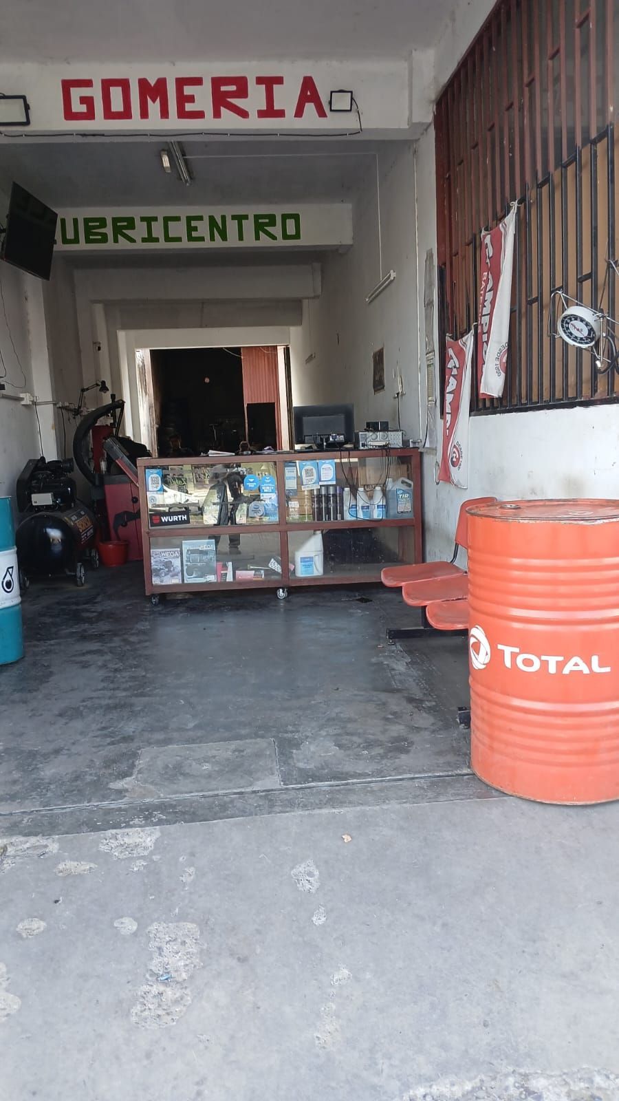 Entrada de una gomería con un bidón de aceite Total al frente y una vitrina en el interior.
