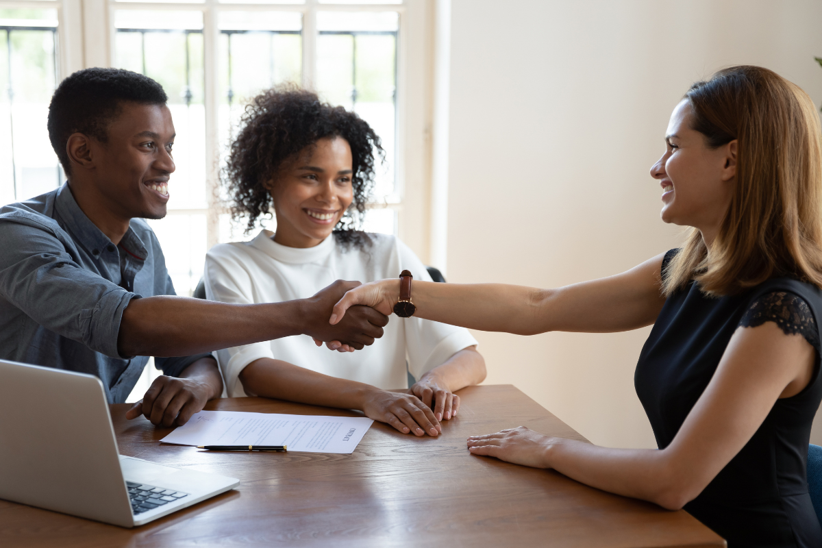Couple talking to mortgage planner and shaking hands across the table