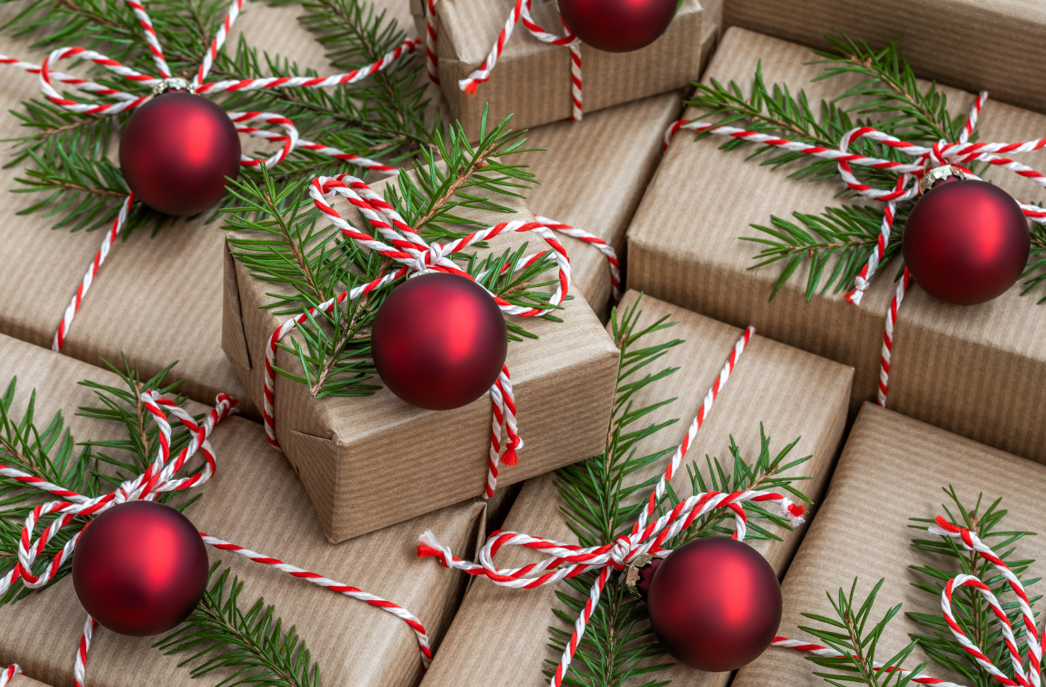 A pile of christmas presents wrapped in brown paper and decorated with red balls and pine branches.