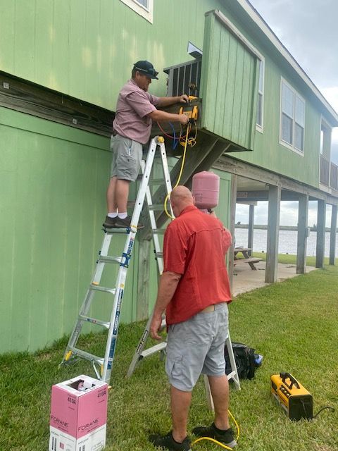 Two men are working on the side of a green house.