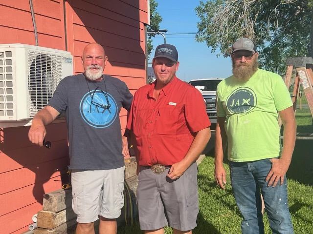 Three men are posing for a picture in front of a red building