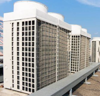 A row of large, white industrial air conditioning units installed on a rooftop against a clear blue sky.