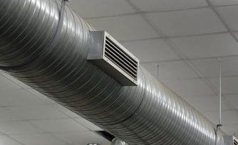 A cylindrical metal HVAC duct suspended from a drop ceiling, featuring a rectangular ventilation register.