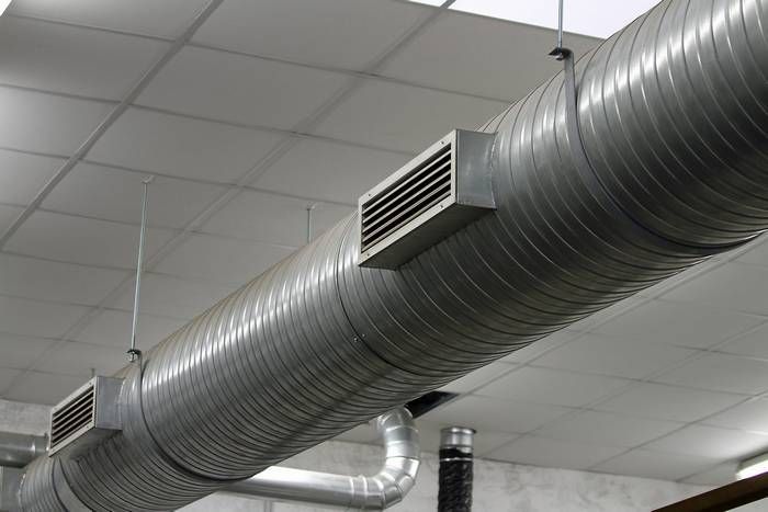 A low-angle view of industrial metal HVAC ducts suspended from a white drop ceiling.