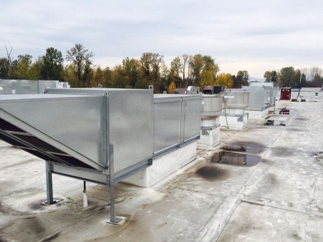 Metal HVAC rooftop units and ventilation equipment installed on a flat commercial roof with trees in the background.