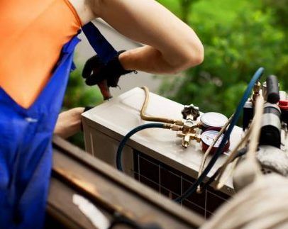 Technician in blue workwear servicing an outdoor air conditioning unit with a manifold gauge set.