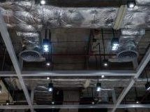 Exposed ceiling with silver insulated ventilation ducts, circular air vents, and suspended pendant lights.