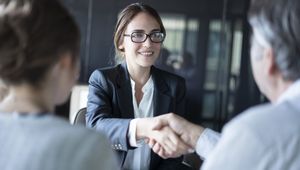 A woman is shaking hands with a man and a woman during a job interview.