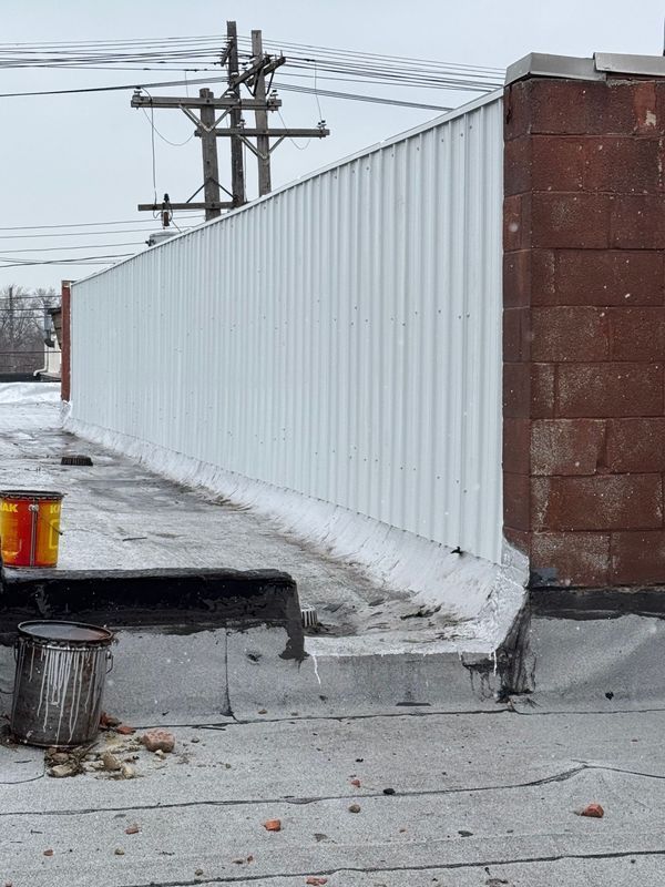 White corrugated metal wall atop a flat roof, next to a brick wall