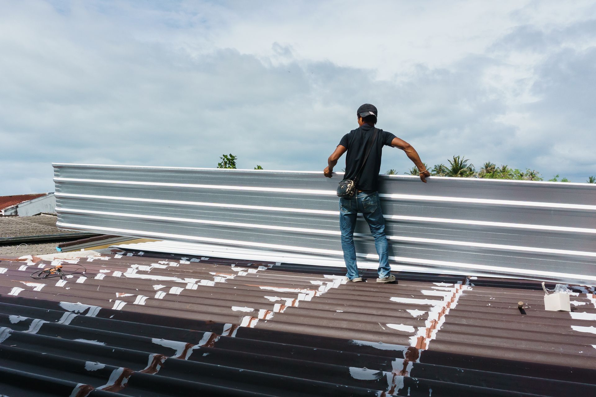 A person installs gray metal roofing panels on a rooftop