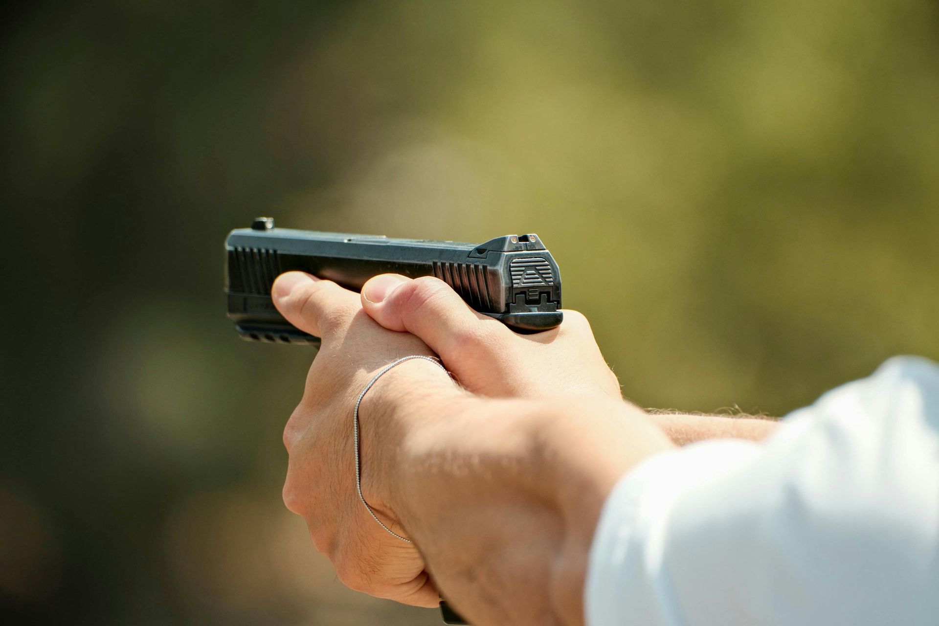 Person aiming a rifle at a shooting range, wearing ear protection, with a scope.